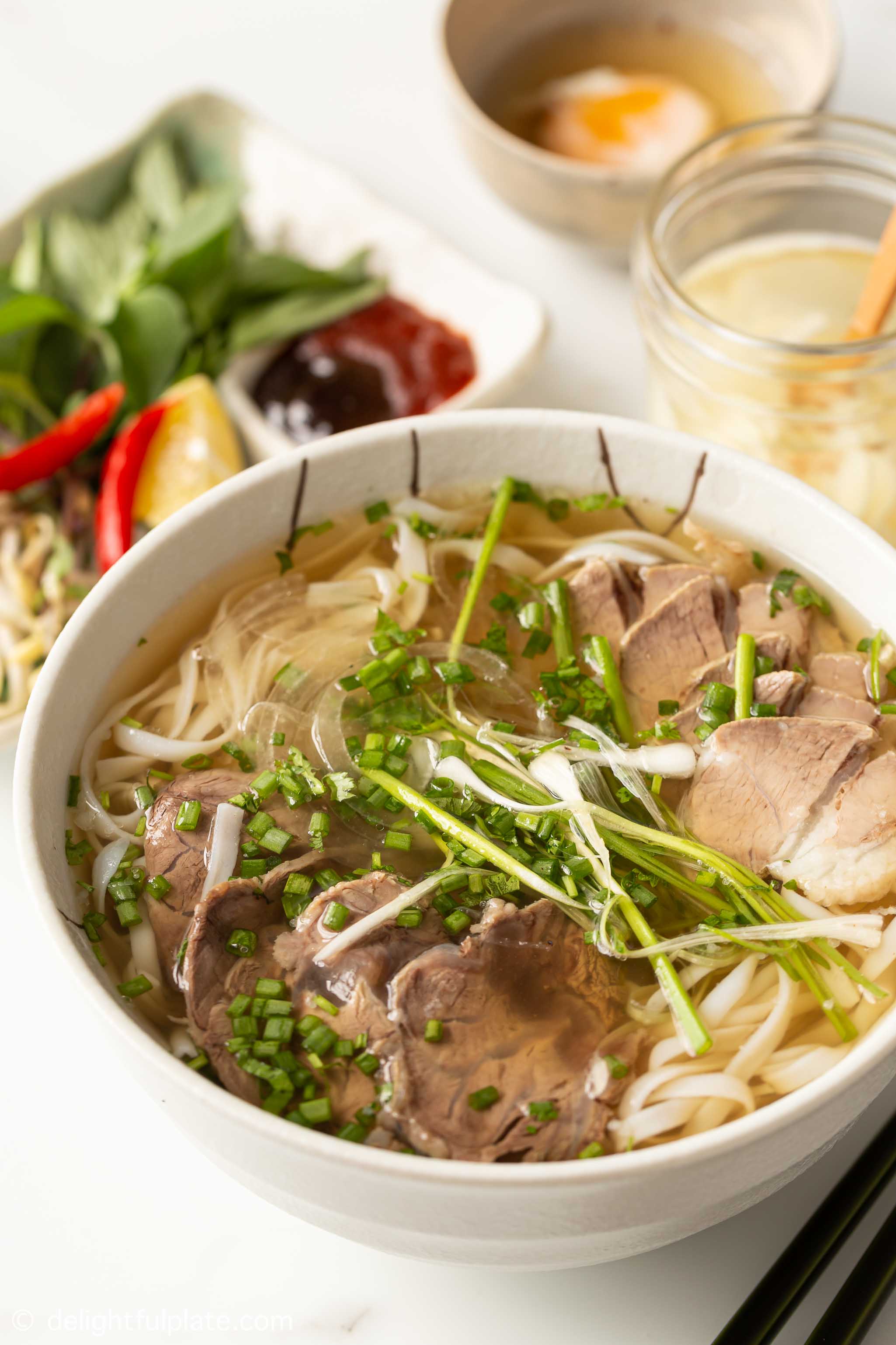 a bowl of Vietnamese beef pho noodle soup served with accompaniments