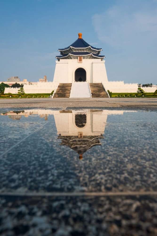 the famous white and blue pagoda in chiang kai shek memorial hall, with a puddle in front of it and reflection in the puddle