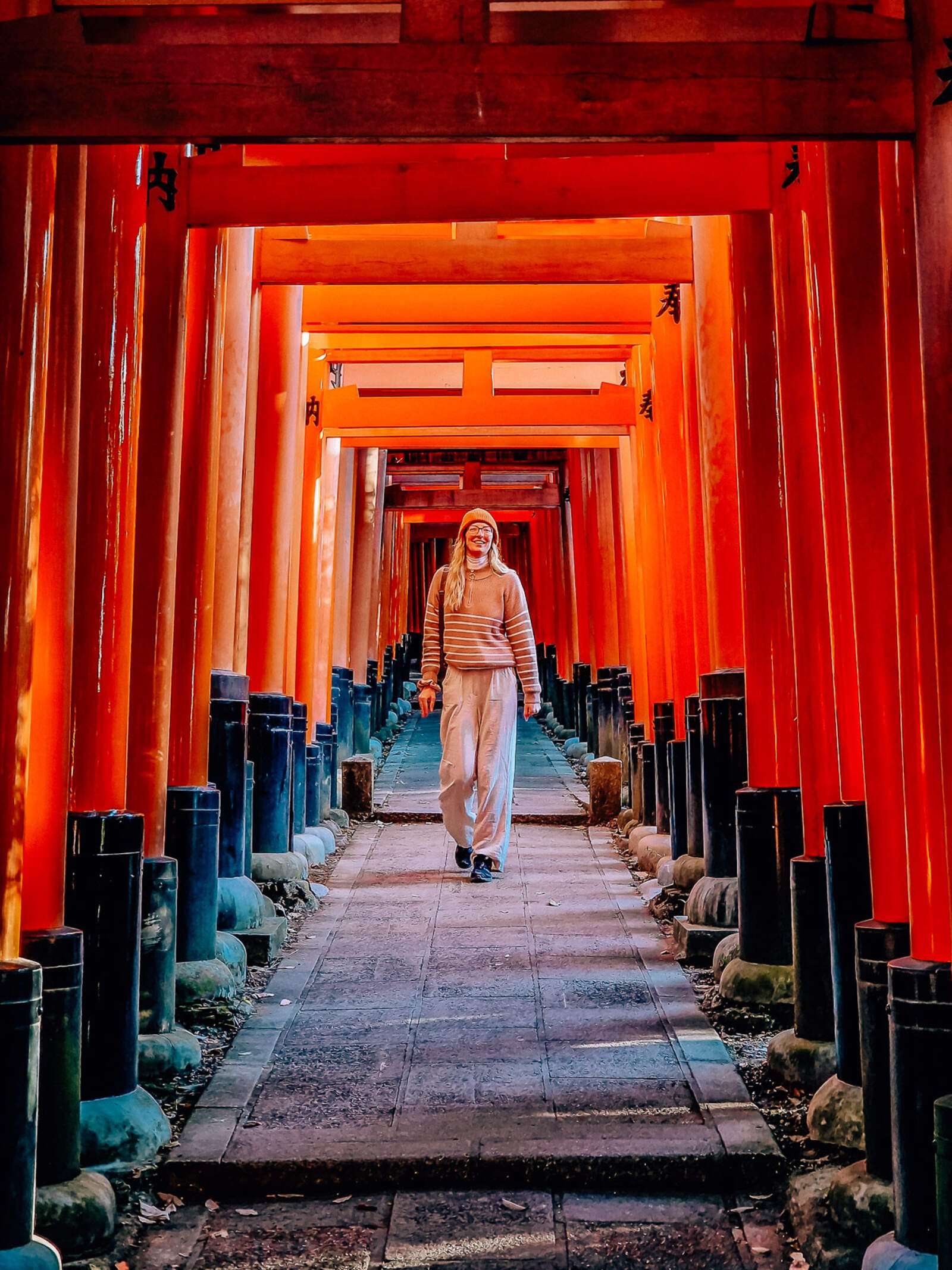 Helena walking down a path with orange arches all the way along - Japanese torii gates